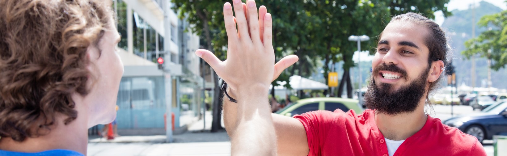 Zwei junge Männer schauen sich fröhlich an und klatschen sich mit der rechten Hand ab