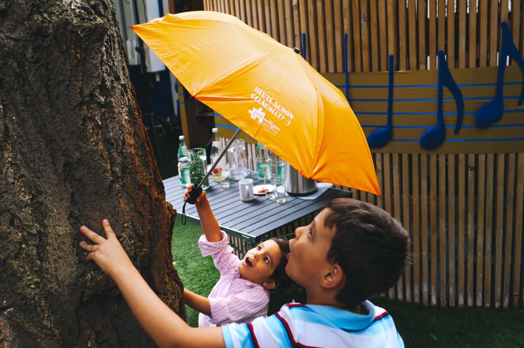Zwei Kinder mit einem Schirm, darauf steht "Freiwilligen-Agentur Halle" - heute schon gelächelt?