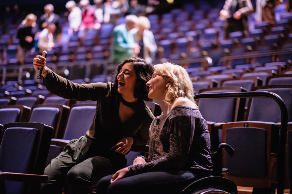 Zwei Frauen sitzen in einem Veranstaltungsraum und machen ein Selfie